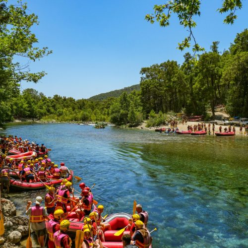 People in red rafts getting ready for river rafting under clear blue sky.